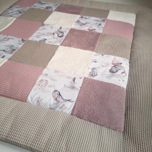 Könnte beinhalten: Eine Patchwork-Baby-Spielmatte mit verschiedenen Texturen und Mustern. Die Spielmatte besteht aus einem hellbraunen Waffelgewebe, einem weißen flauschigen Stoff und einem rosa Frottee. Die Spielmatte zeigt auch verschiedene bedruckte Stoffe mit Meeresbewohnern, darunter Wale, Narwale und ein Tintenfisch.