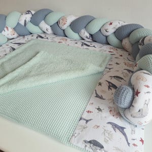 Könnte beinhalten: Ein hellgrüner und grauer geflochtener Stoßfänger mit einer weißen und hellgrünen Waffel-Decke und einem weißen Laken mit einem Meereslebewesen-Druck.