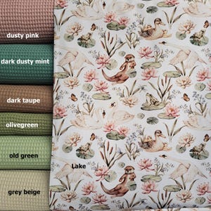 May include: White fabric with a repeating pattern of swans, otters, frogs, butterflies, water lilies, and reeds. The fabric has a light green, pink, and brown color scheme. The text "Lake" is printed on the fabric.