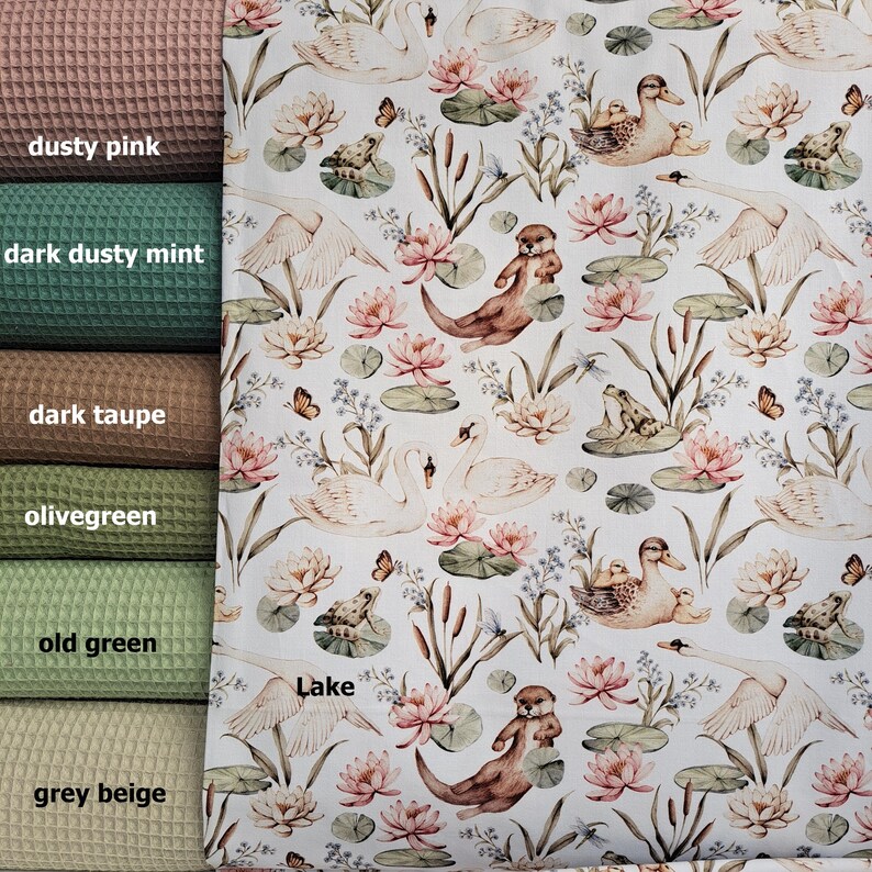 May include: White fabric with a repeating pattern of swans, otters, frogs, butterflies, water lilies, and reeds. The fabric has a light green, pink, and brown color scheme. The text "Lake" is printed on the fabric.