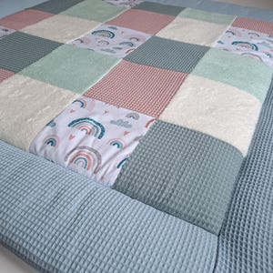 Könnte beinhalten: Eine Patchwork-Baby-Spielmatte mit verschiedenen Texturen und Farben. Die Spielmatte hat ein hellblaues, weißes, rosa und grünes Farbschema. Die Spielmatte ist aus weichem, bequemem Stoff gefertigt und perfekt für Babys zum Spielen.