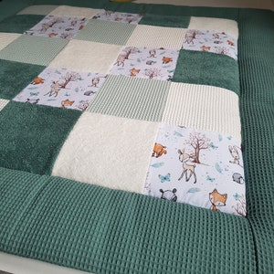 Könnte beinhalten: Eine grüne und weiße Patchwork-Spielmatte mit Waldtier-Motiv. Die Spielmatte ist aus weichem, strukturiertem Stoff gefertigt und zeigt verschiedene Tiere, darunter Rehe, Füchse und Kaninchen.