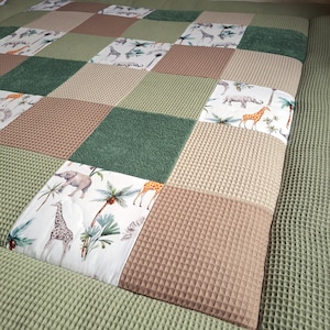 Könnte beinhalten: Eine Patchwork-Spielmatte in Grün, Braun und Weiß. Die Spielmatte zeigt verschiedene Tiermotive, darunter Giraffen, Elefanten und Palmen.