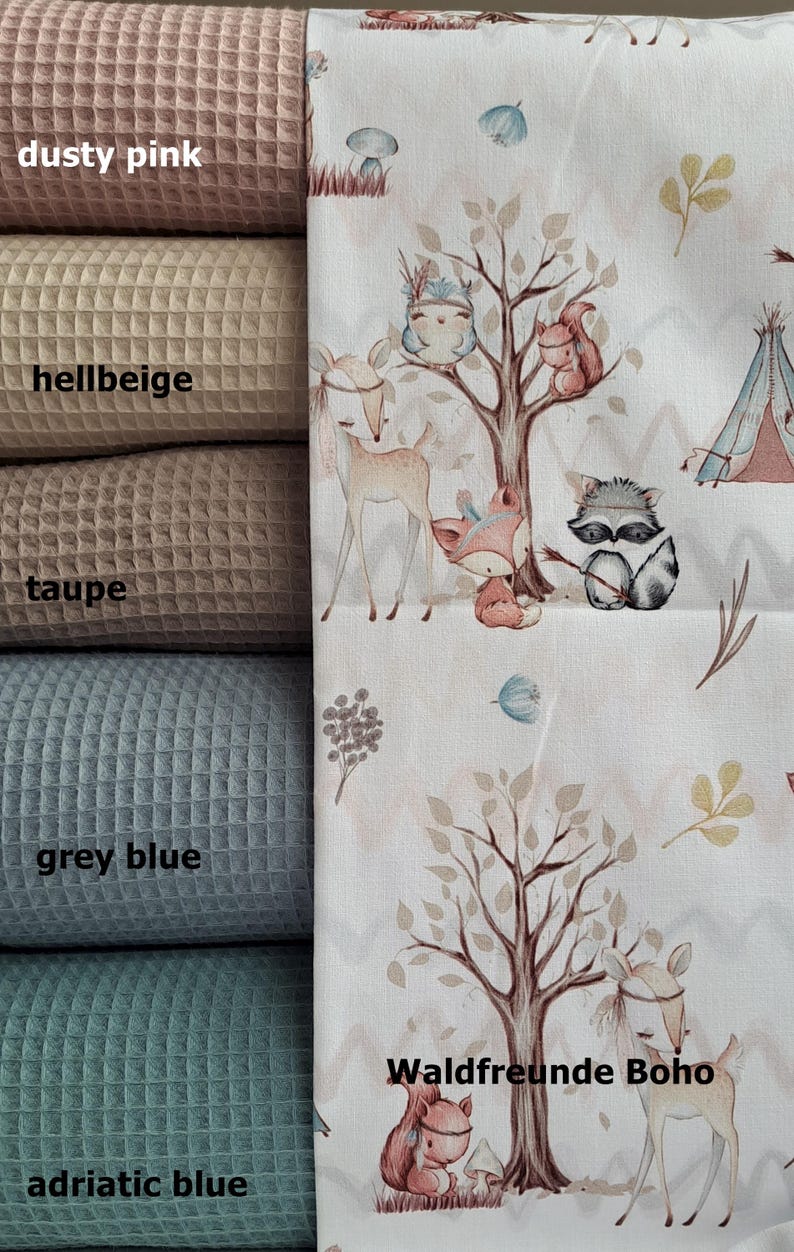 May include: Five fabric swatches in different colors: dusty pink,  hellbeige, taupe, grey blue, and adriatic blue. The swatches are arranged vertically, with the dusty pink swatch at the top and the adriatic blue swatch at the bottom.  A white fabric with a woodland animal print is shown to the right of the swatches. The print features a tree with a fox, a raccoon, a deer, and a squirrel. The text "Waldfreunde Boho" is printed on the fabric.