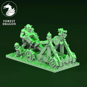 May include: A green miniature catapult model with goblin figures. The model features wooden beams, wheels, and decorative elements. The base is covered in green grass. The Forest Dragon logo is in the upper left corner.