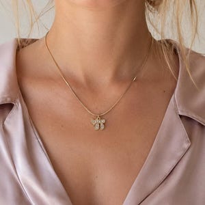May include: A gold-toned chain necklace featuring a small pendant shaped like the Hebrew letters Chai, which are encrusted with small, clear, sparkling stones. The necklace rests against a light pink satin collared shirt with a visible button placket.