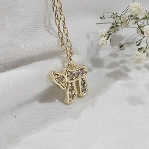 May include: A gold-toned necklace featuring a pendant shaped like the Hebrew letter Chai, encrusted with small clear stones. The pendant hangs from a delicate gold-toned chain, showcasing a polished metallic finish and a reflective, sparkling surface.
