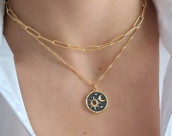 May include: A gold chain necklace with a sun and moon pendant. The pendant is black with gold accents and a red gemstone in the center of the sun.