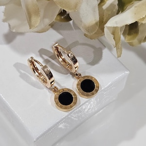 May include: Gold hoop earrings with a black enamel circle pendant featuring Roman numeral markings.