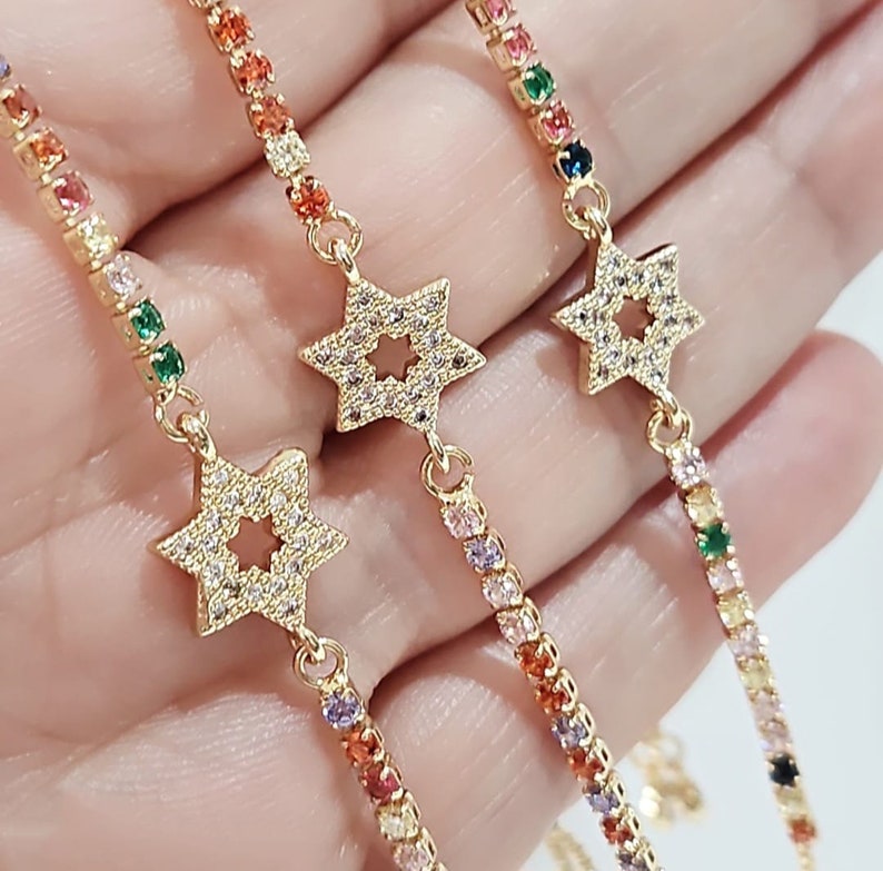 May include: Three gold bracelets with colorful crystal accents and a star charm. Each bracelet features a different color scheme.