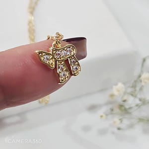 May include: A gold-toned pendant shaped like the Hebrew letter Chai, featuring a polished metal finish and embedded with small, clear, sparkling stones. The pendant is attached to a delicate gold-toned chain, showcasing a reflective surface.