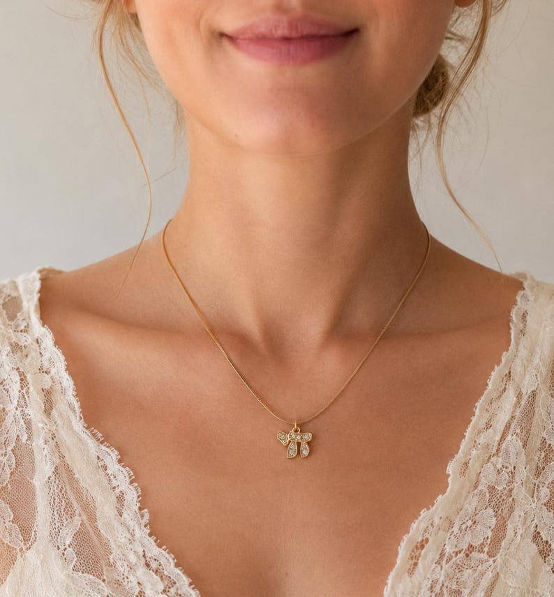 May include: A gold-toned necklace featuring a small pendant shaped like the Hebrew letter Chai, which is encrusted with small, clear, sparkling stones. The pendant hangs from a delicate, thin gold-toned chain that rests against the collarbone area.