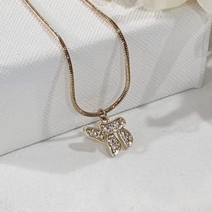 May include: A gold-toned snake chain necklace featuring a pendant shaped like the Hebrew letter Chai. The pendant is embellished with small, clear, sparkling stones set into the metal surface, creating a bright and reflective appearance.