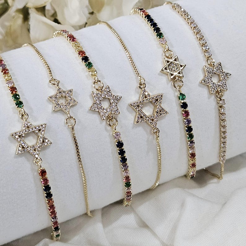May include: Five gold chain bracelets with a star of David charm. Each bracelet features a different colored chain with small gemstones.