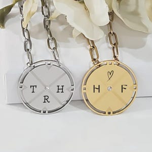 May include: Two silver and gold necklaces with round pendants. The silver pendant has the letters "THR" with a small diamond in the center. The gold pendant has the letters "HF" with a small diamond in the center and a heart symbol above the letters.