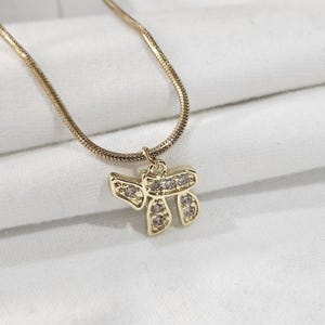 May include: A gold-toned snake chain necklace featuring a pendant shaped like the Hebrew letter Chai. The pendant is embellished with small, clear, sparkling stones set into the metal frame, creating a bright and reflective appearance.