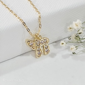 May include: A gold-toned necklace featuring a pendant shaped like the Hebrew letter Chai, encrusted with small clear stones. The pendant hangs from a delicate gold-toned chain, showcasing a polished finish and a reflective, metallic appearance.