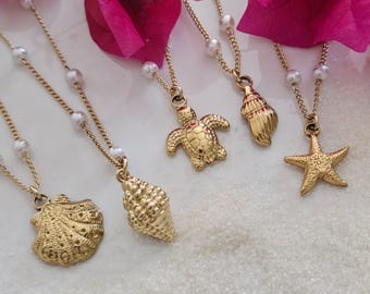 May include: Five gold necklaces with pearl accents and different sea-themed charms, including a seashell, a starfish, a turtle, and a conch shell. The necklaces are displayed on a white surface.