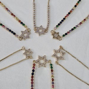 May include: Six gold chain bracelets with a star of David charm. Each bracelet has a different colored chain, including rainbow, black, and white.