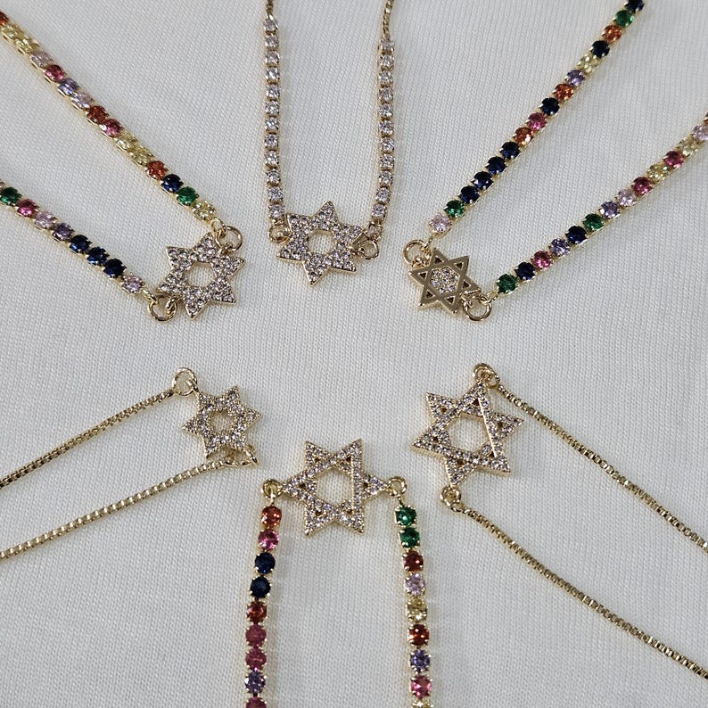 May include: Six gold chain bracelets with a star of David charm. Each bracelet has a different colored chain, including rainbow, black, and white.