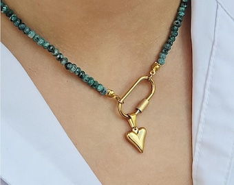 May include: A gold necklace with a heart pendant and a carabiner clasp. The necklace is made of small, green gemstone beads.