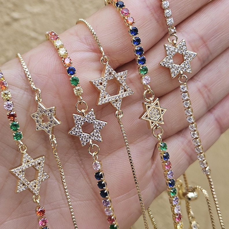 May include: Five gold chain bracelets with a star of David charm. Each bracelet features a different colored chain with small gemstones. The chains are adjustable.