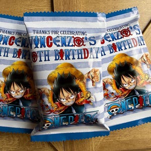 Puede incluir: Tres bolsas de regalo para fiestas con un diseño de rayas azules y blancas. Cada bolsa presenta un personaje de dibujos animados de One Piece, el texto "Gracias por celebrar el 10º cumpleaños de Vincenzo" y el logo de One Piece.