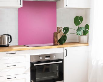May include: A kitchen scene featuring a vibrant pink backsplash panel installed behind a stainless steel oven and stovetop. The kitchen includes white cabinets, a wooden countertop, a silver electric kettle, and a green potted plant.