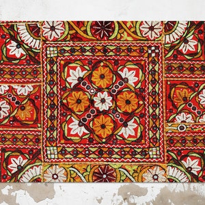 May include: A red, white, and yellow embroidered textile with a geometric pattern. The textile is made up of several squares with different designs. The textile is framed and hanging on a wall.