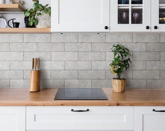 May include: A kitchen scene featuring white cabinets with black handles, a light wood countertop, and a gray subway tile backsplash. A wooden knife block, a small potted plant in a woven basket, and open shelving with decor are visible.