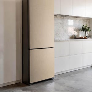 Può includere: Un frigorifero beige con una cornice grigio scuro in una cucina moderna. Il frigorifero ha due porte, una superiore e una inferiore, con una maniglia nera orizzontale. Sono visibili anche mobili bianchi e un paraschizzi in marmo.