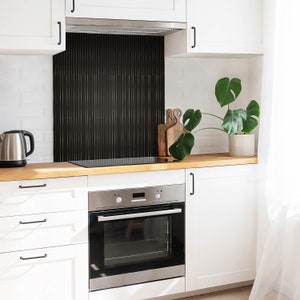 Puede incluir: Una cocina moderna con gabinetes blancos y un protector contra salpicaduras de azulejos negros y dorados. La cocina cuenta con un horno de acero inoxidable y una encimera de madera.