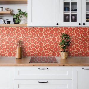 Könnte beinhalten: Eine weiße Küche mit einer Rückwand aus roten Grapefruit-Scheiben. Die Arbeitsplatte ist aus Holz und hat ein schwarzes Elektrokochfeld. Unter der Arbeitsplatte befinden sich weiße Schränke.