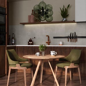 May include: A round wooden dining table with two olive green upholstered armchairs featuring wooden legs. Above the table hangs a multi-globe olive green glass pendant light. The kitchen features dark wood cabinetry, a copper faucet, and a magnetic knife rack.