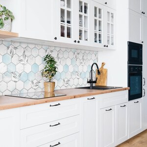 May include: A contemporary kitchen featuring white cabinets, a wooden worktop, and a black sink and tap. The backsplash showcases hexagonal tiles with a leaf design and blue highlights. A small potted plant is on the worktop.