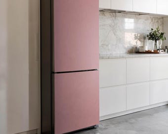 Puede incluir: Un refrigerador de dos puertas con acabado rosa mate. El refrigerador tiene un marco gris oscuro y está colocado contra una pared blanca y gabinetes de cocina. La cocina tiene una placa para salpicaduras de mármol y un piso de concreto.
