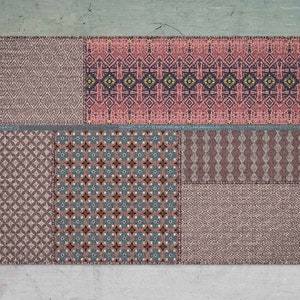 Può includere: Un tappeto patchwork con una varietà di motivi geometrici in tonalità di rosa, blu e grigio.