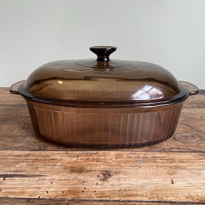 May include: A brown glass oval baking dish with a lid. The dish has a ribbed design and a knob on the lid.