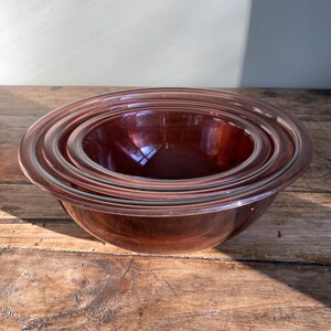 May include: Set of four nesting glass mixing bowls in a deep burgundy colour. The bowls are clear glass with a burgundy tint.