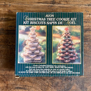 May include: A square box for an Avon Christmas Tree Cookie Kit featuring two images of stacked star-shaped cookies shaped like trees. The dark green packaging includes the text AVON CHRISTMAS TREE COOKIE KIT and instructions to bake, stack, and decorate.