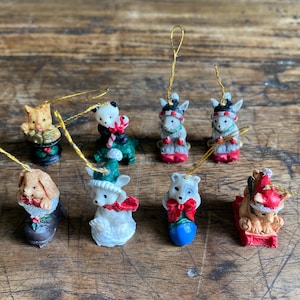 May include: A collection of eight miniature animal ornaments with gold hanging strings. The figures include a cat, a panda with a candy cane, two grey mice, a rabbit in a boot, a white bear in a green hat, a bear with a red bow, and a bear on a sled.