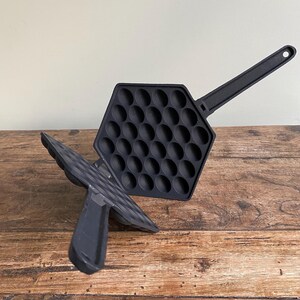 May include: Black cast iron Hong Kong egg waffle maker. The hexagonal waffle iron has a long handle and a series of round indentations for cooking. The waffle maker is open, revealing the cooking surface. The handle has a hole for hanging.