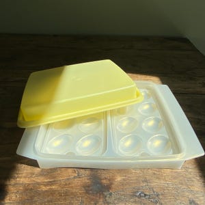 Peut inclure: Un ancien récipient à œufs en plastique. Il se compose d'un plateau transparent avec des alvéoles en forme d'œufs et d'un couvercle jaune. Le récipient est conçu pour contenir une douzaine d'œufs.