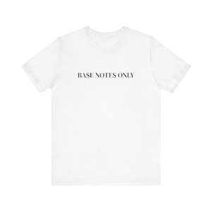 Może przedstawiać: Biały t-shirt z czarnym napisem "BASE NOTES ONLY". Koszulka ma krótkie rękawy i okrągły dekolt, prawdopodobnie wykonana z bawełny. Tekst jest wyśrodkowany na piersi.