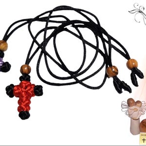 May include: Two knotted crosses, one red and one purple, hang from a black cord with wooden beads. The cord is tied in a loop at the end.