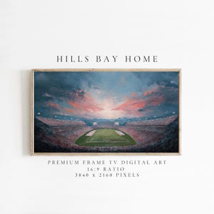 Op de afbeelding: Een ingelijste digitale kunstprint met een voetbalstadion bij zonsondergang. Het kunstwerk toont een groen veld, gevulde tribunes en een levendige lucht met tinten blauw, oranje en rood. De tekst "HILLS BAY HOME" staat bovenaan.