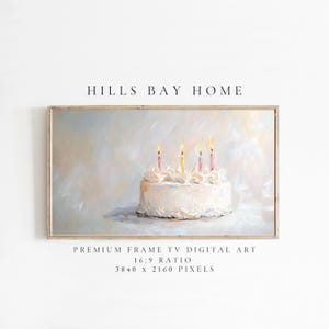 Puede incluir: Un pastel blanco con glaseado rosa y blanco y velas encendidas. El pastel está sobre una superficie blanca con un fondo azul claro. La imagen está enmarcada con un marco de madera claro.