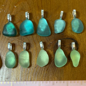 Op de afbeelding: Tien hangers van zeeglas met zilveren springringen. Het zeeglas is in tinten groen en turquoise.