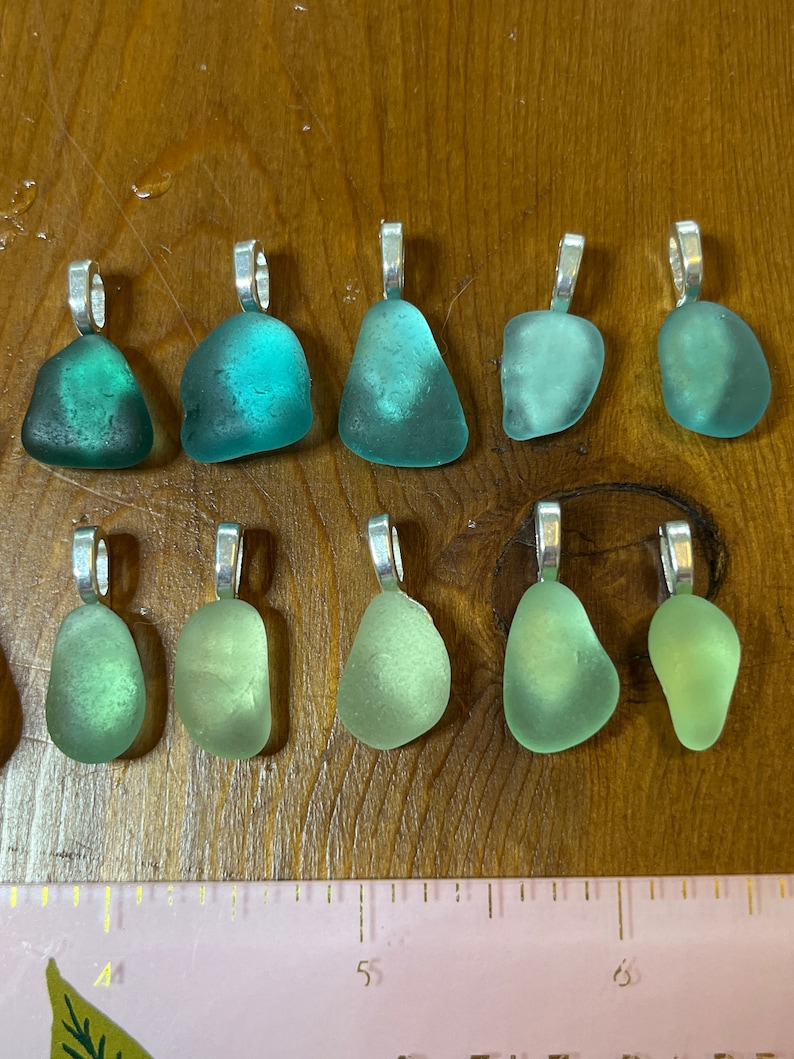 Op de afbeelding: Tien hangers van zeeglas met zilveren springringen. Het zeeglas is in tinten groen en turquoise.