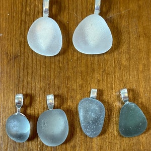 Op de afbeelding: Zes  zee-glas hangers met zilveren springringen. Twee zijn helder, twee zijn wit en twee zijn groen.